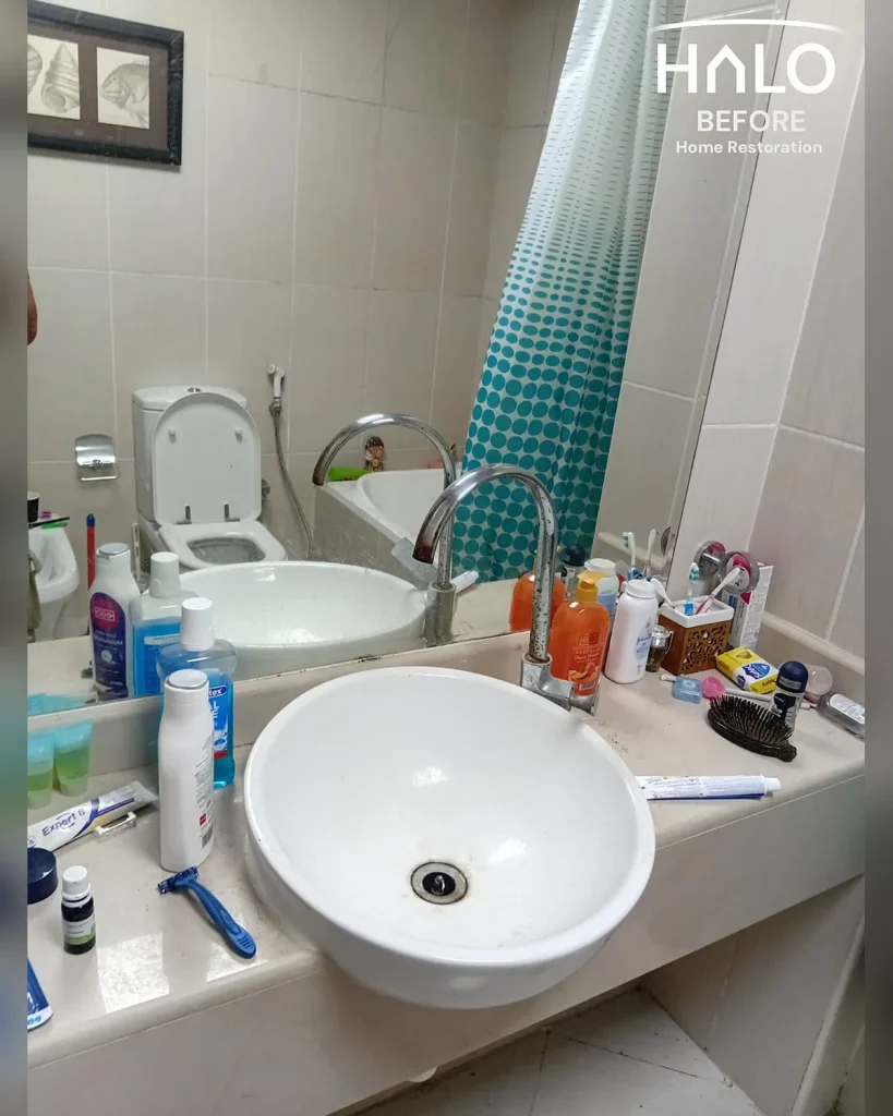 Before a bathroom deep clean in Ras Al Khaimah - basin ringed with grime and limescale, the vanity crowded with toiletry bottles