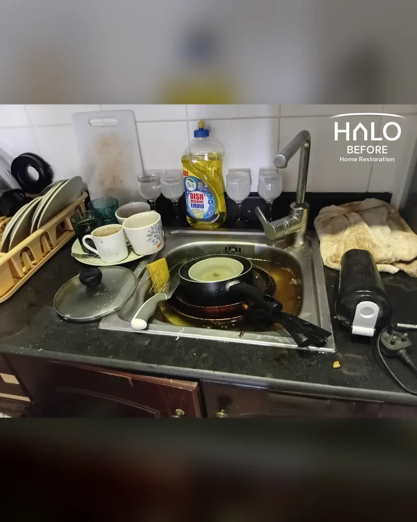 Before a home restoration clean in Ras Al Khaimah - kitchen sink piled high with dirty dishes, greasy pans and unwashed glasses on a grimy worktop