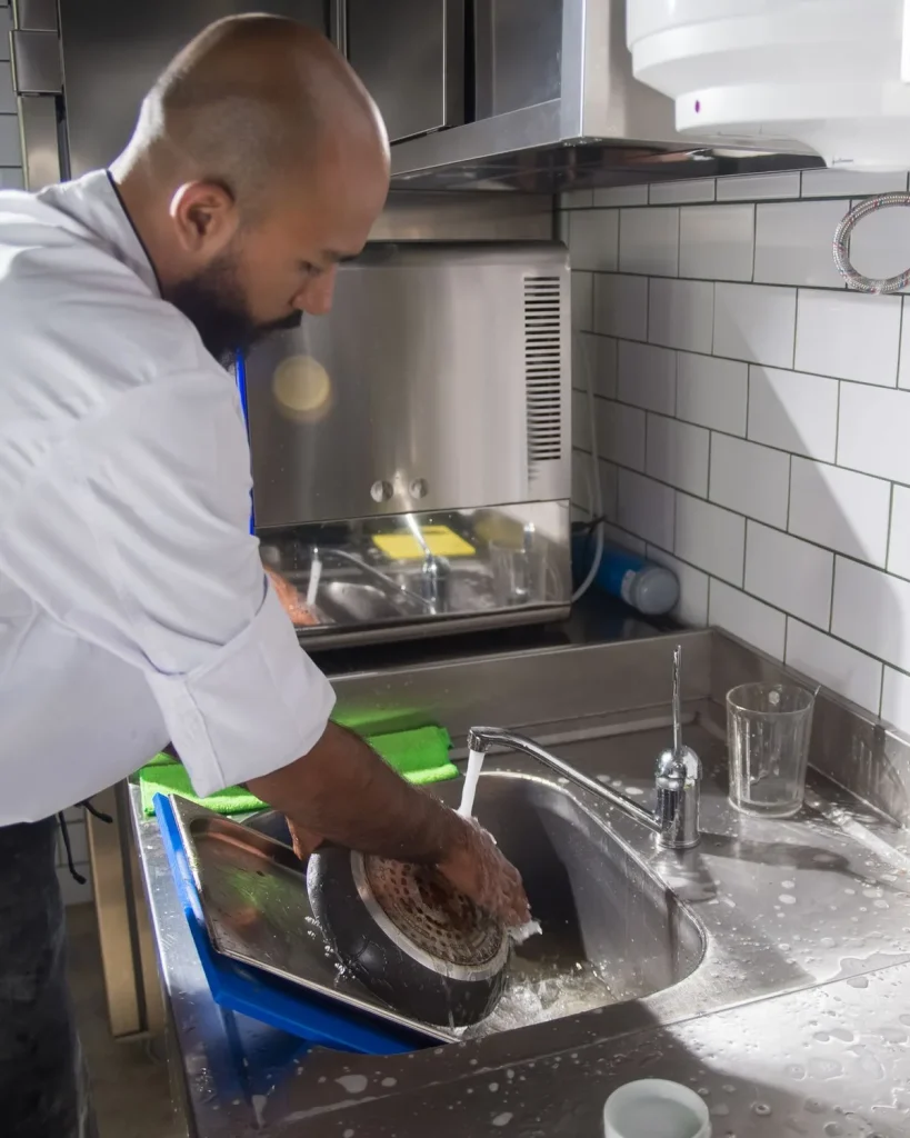 Chef washing a pan in a stainless steel commercial kitchen sink after service