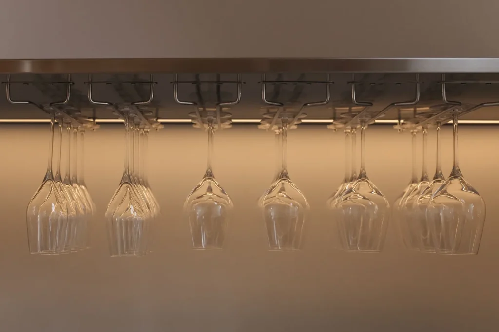 Rows of clean wine glasses hanging rim down on a stainless steel rack, the way glassware is stored after washing