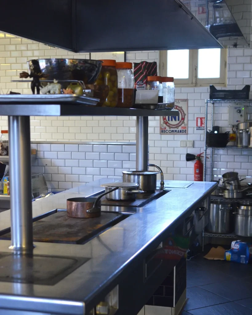 Stainless steel cooking line under an extraction canopy in a commercial restaurant kitchen, the surfaces a restaurant deep clean strips back to bare steel